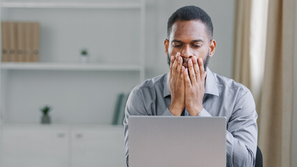 Stressed shocked African American ethnic bearded adult man office worker businessman with laptop...