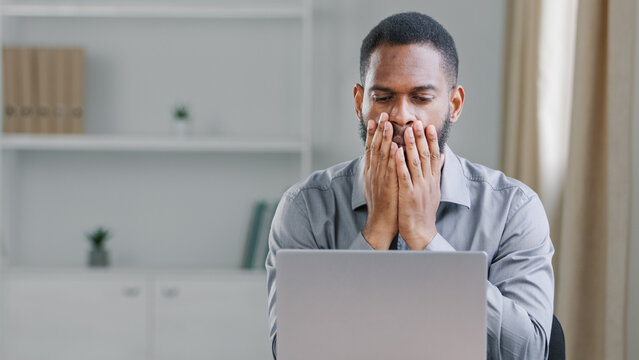 Stressed shocked African American ethnic bearded adult man office worker businessman with laptop computer sad upset frustrated reading online bad news mistake service error failure business problem
