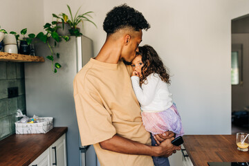 Affectionate father giving his daughter a forehead kiss at home