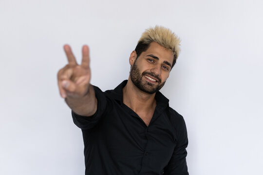Cheerful businessman showing peace sign. Male Caucasian model with brown eyes, ombre painted hair and beard in black shirt smiling making victory sign. Confidence, self-assurance concept