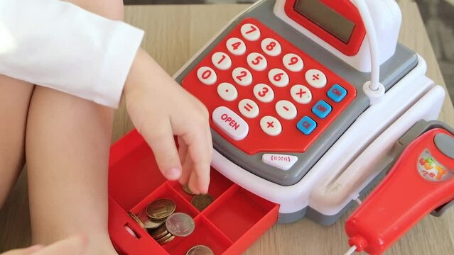 The kid plays a children's toy. Puts the coins in the cash register. Playing like he is in the store. Sells or buys something.