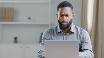 Confused puzzled African American ethnic bearded man reading bad news bank notice work with online project has difficult task office worker businessman with laptop computer failure business problem