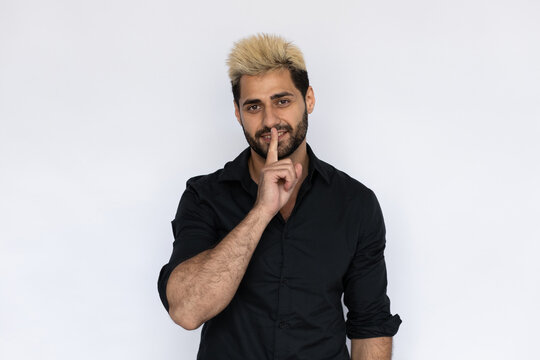 Playful businessman showing hush gesture. Male Caucasian model with brown eyes, ombre painted hair and beard in black shirt making shhh gesture. Secret, silence concept