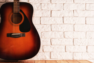 Wooden table with an acoustic guitar and white bricks background. Abstract music and sound backdrops. Copy space for text