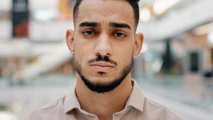 Close-up of face upset young man sad frustrated millennial guy looking at camera serious hispanic male having negative thoughts depressive mood difficult period life misunderstanding problems at work