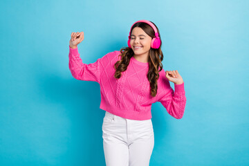 Photo of young dancing satisfied teenager schoolgirl wear new wireless pink headphones hands up active dance isolated on blue color background