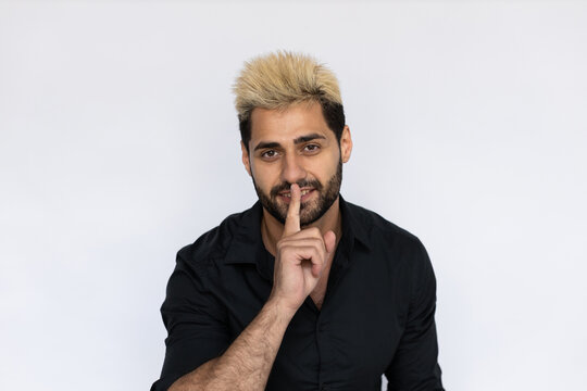 Portrait of playful businessman showing hush gesture. Male Caucasian model with brown eyes, ombre painted hair and beard in black shirt making shhh gesture. Secret, silence concept