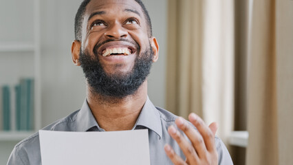 Happy ethnic winner office worker African businessman ethnic bearded American male manager entrepreneur employer man reading letter mail with invite to new job paper notice victory bank loan agreement