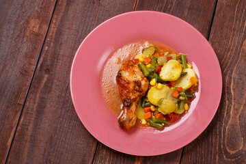 Baked chicken drumstick with vegetables in sauce and spices on a wooden table.