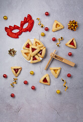 Hamantaschen Cookies, Triangular Pastry, Red Carnival Mask, Noisemaker on Gray Stone Table. Purim Celebration, Jewish Carnival Holiday Concept.