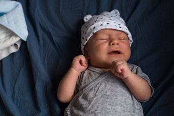 Newborn baby boy in white cap making faces
