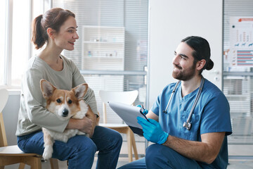 Young male veterinarian with medical document talking to owner of pet
