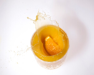 slice of orange splashing into a glass of orange juice from above