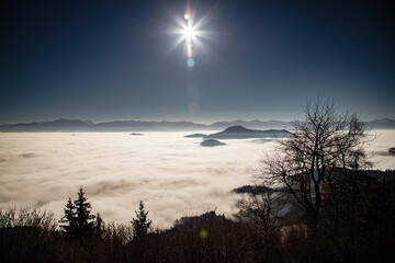 the sun standing high in the sky above a sea of clouds during a inversive weather situation in carinthia austria.