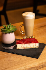 Latte coffee with strawberry cheesecake on wooden table in coffeeshop on black platter