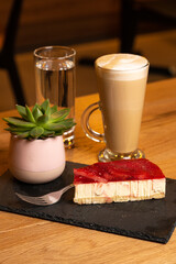 Latte coffee with strawberry cheesecake on wooden table in coffeeshop on black platter