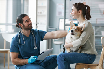 Happy young veterinarian in gloves and uniform consulting pet owner
