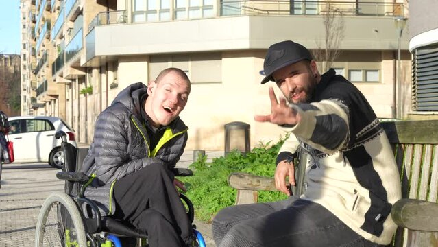 Portrait of disabled person in wheelchair with friend sitting having fun in the street