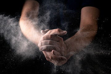 Fototapeta na wymiar Explosion of flour in male hands on a dark background. Dough preparation, cooking concept.