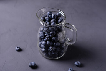 Blueberries in a glass jug on a gray concrete background. The benefits of berries, vegetarianism concept.