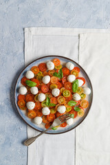 Isolated plate of tomato salad with tuna fish, mozzarella cherries, and basil leaves.  Flat lay