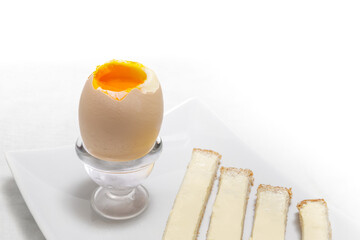 Close-up of one soft half-boiled egg. It is on a stand, isolated on white background. The top is open like a lid and shows delicious orange yolk. Called "Oeuf a la coque" in French.