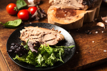 Chopped baked piece of meat with raw vegetables on a wooden background.