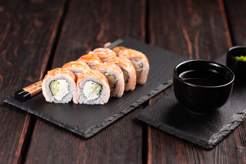 Japanese kitchen - sushi roll with cucumber and cream cheese topped with shrimp on black board