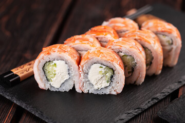 Japanese kitchen - sushi roll with cucumber and cream cheese topped with shrimp close-up on black board