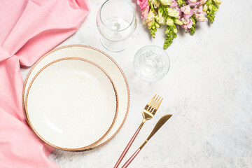 Spring or summer table setting with plate, flowers and cutlery at white kitchen table. Top view.
