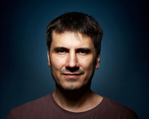 Fototapeta premium Portrait of a 42-year-old brunette man on a dark background with bright illumination