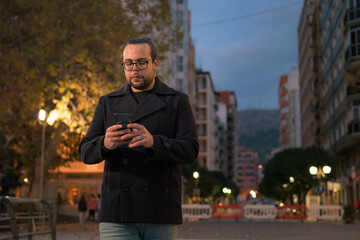 Man walks and looks at his phone on the street at night