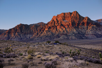 Lever de soleil sur Red Rock Mountain, Las Vegas, Nevada, États-Unis d'Amérique. Montagne à la roche rouge bordant une plaine aride de cailloux et buissons secs.