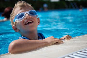 Boy cheerfully swims in the children's pool, dives in swimming glasses. Summer entertainment of a...
