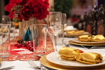 Table de fête avec couverts et verres de luxe, serviettes dorées, nappe blanche et napperon brodé rouge. Décoration de Noël et roses rouges.