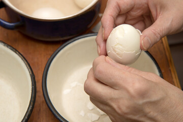 hands of a middle-aged woman peeling a boiled egg from the shell