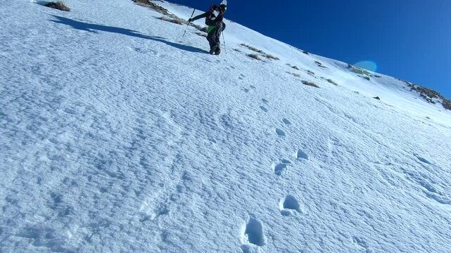 man hiking a snowy steep slop with sticks and a splitboard on the backpack. A technique call Bootpacking (dig steps in hard snow).Follow cam
