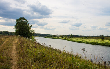 A beautiful pastoral landscape - the bend of the Klyazma River among the picturesque banks in the Moscow region with green grass and trees and a cloudy sky and a space to copy