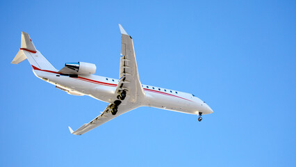 Avion jet privé volant en phase de descente, trains d'atterrissage sortis. Avion à réacteurs blanc et rouge sur fond de ciel bleu.