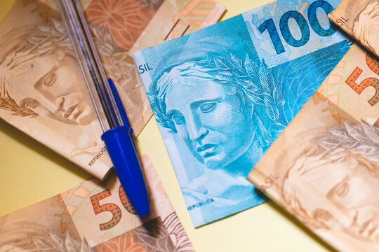 Notas do Real Brasileiro em fotografia macro. Fundo com papel amarelo e uma caneta na composição. Economia brasileira e finanças.