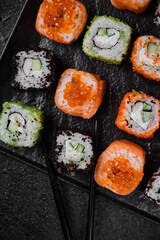 Different kind of sushi roll on on black plate on black concrete 