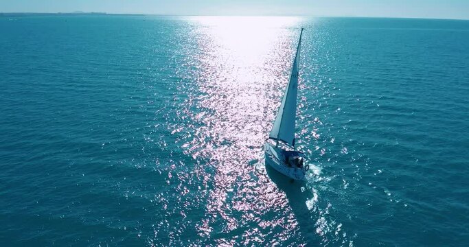 Aerial footage, rear view of luxury sailboat sailing on a deep blue sea with white wakes. Camera follow sailboat in blue ocean water