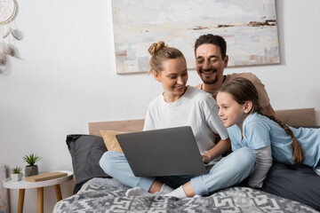 positive parents and happy kid looking at laptop in bedroom.