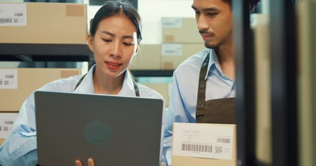 Asian business partner girl hold laptop and man wear formal shirt hold cardboard box training inventory online stock data program for delivery customer at warehouse. Startup small business concept.