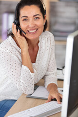 Fototapeta friendly middle aged woman wearing head set in an office obraz