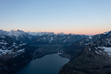 Fototapeta na wymiar Great drone photo in the Swiss Alps over a lake called Walensee and in the background the peaks of the mountains are lit up by the morning sun.