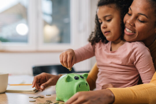Close-up view of mother and daughter putting coins in a piggy bank