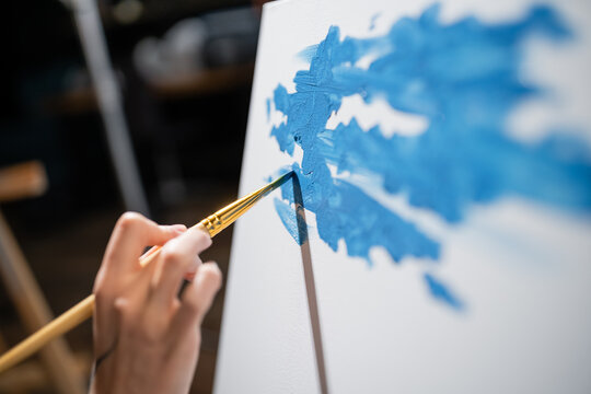 Cropped view of artist painting on canvas in workshop
