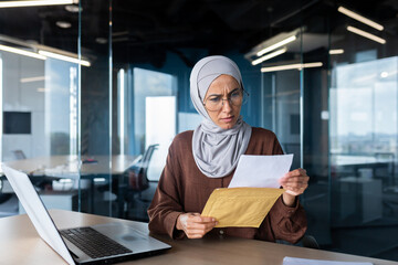 Upset business woman in hijab working inside office, woman received letter envelope mail with bad...