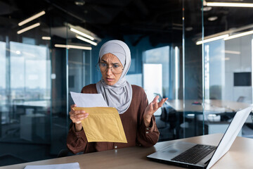 Upset business woman in hijab working inside office, woman received letter envelope mail with bad...